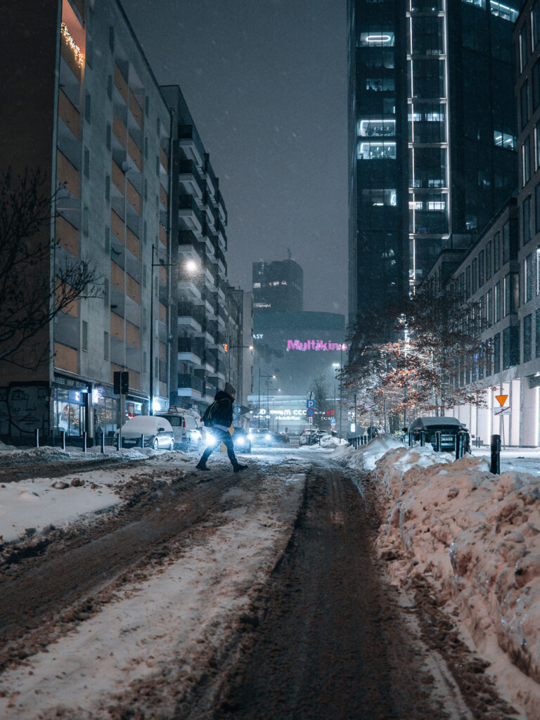 A woman crossing a street during snowfall.