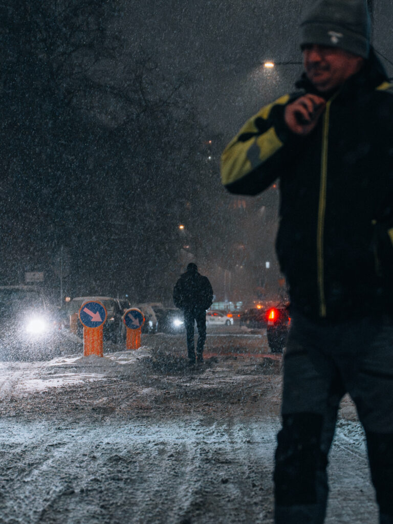 People walking in the middle of the street during snowfall.