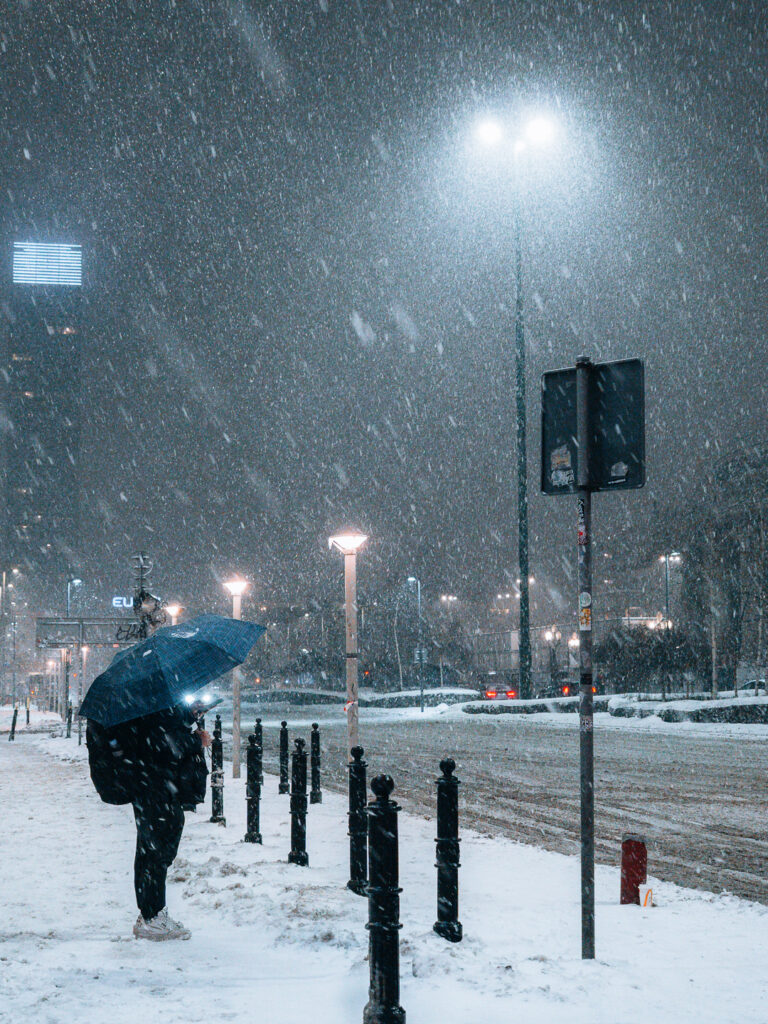 A guy holding an umbrella to protect himself from the snow.