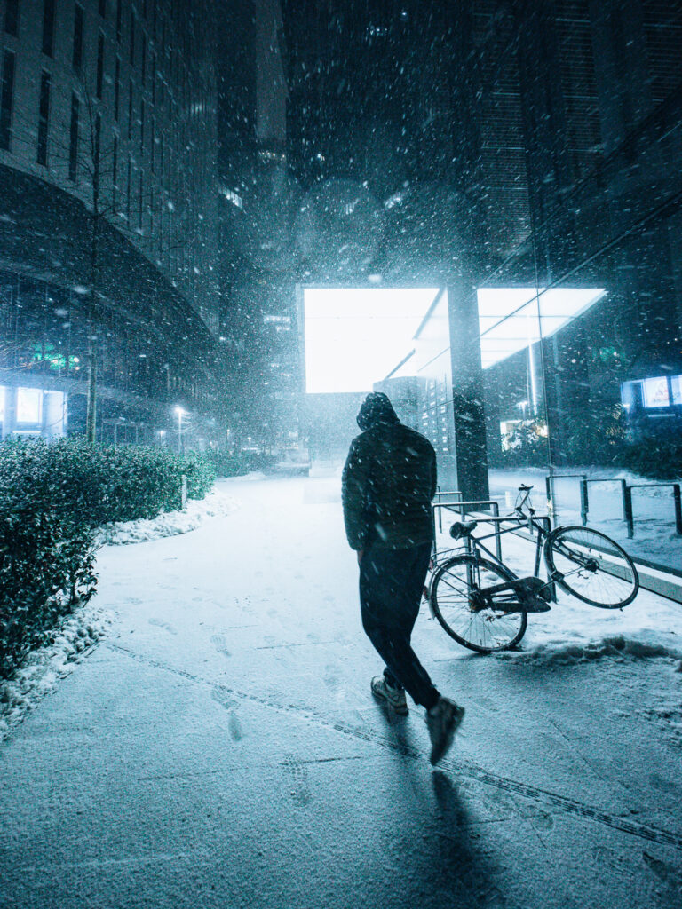 A dark silhouette in motion during snowfall.