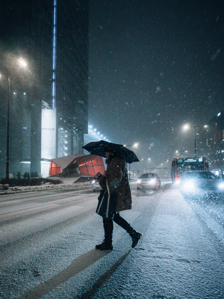 An old lady with an umbrella protecting herself from the snow.