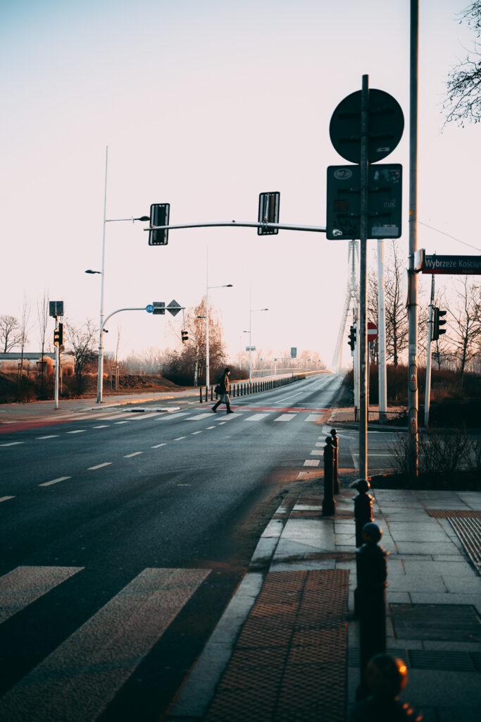 A man crossing the street with the bridge in the back.