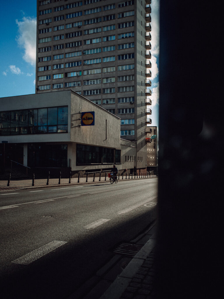 Big scale of the building in the back and a biker on the street.