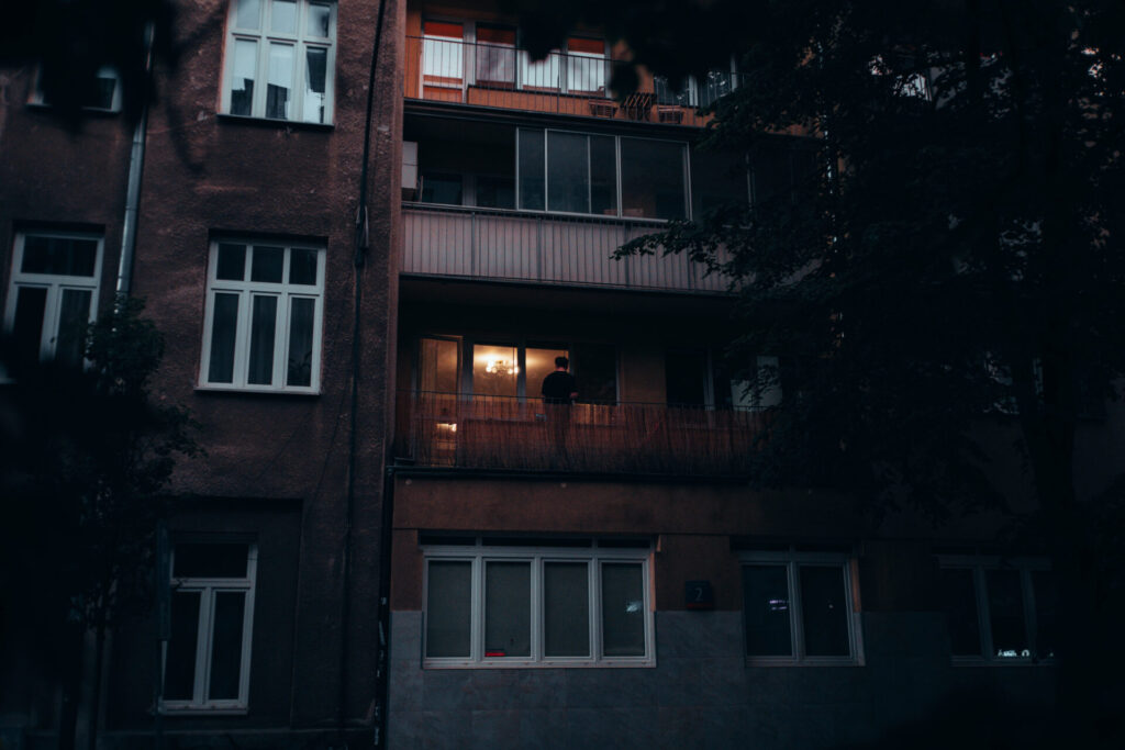 Ambient light coming out from the window with a dude on a balcony, during rainy day in Warsaw.