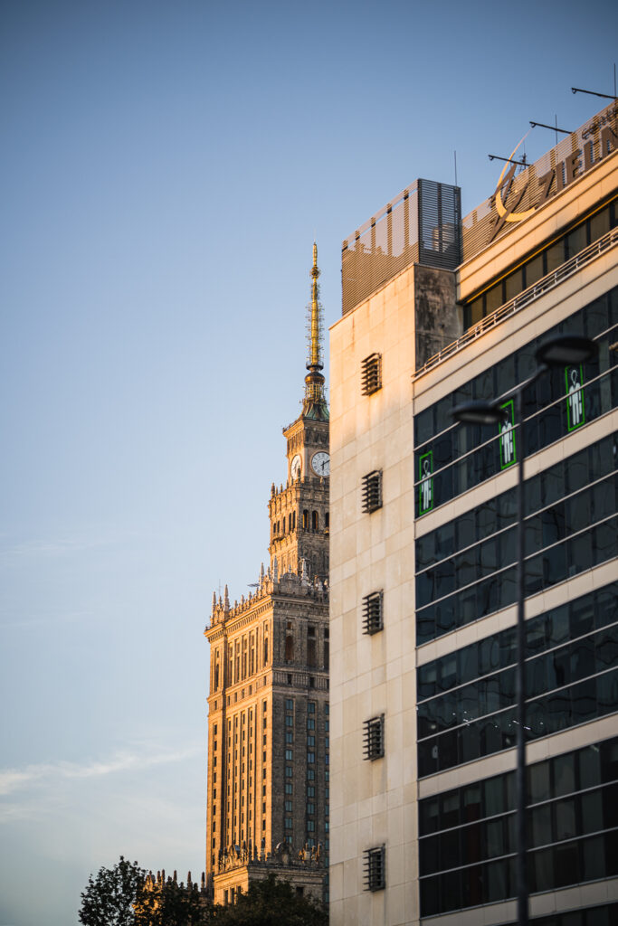 Palace of Culture and Science tower peeking out beside a modern office building in Warsaw at golden hour