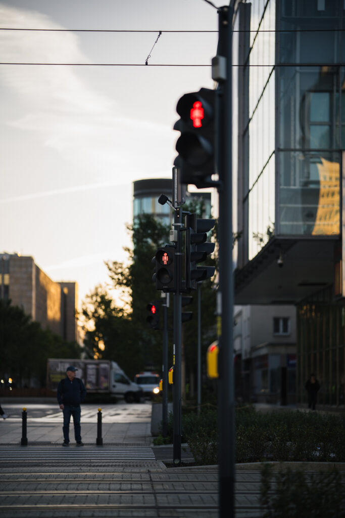 Row of red pedestrian lights at a Warsaw crossing at golden hour, a man waiting at the curb, compressed by the Sigma 85mm F1.2